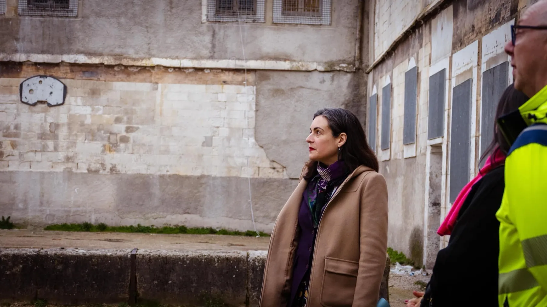 Portrait d'une femme en manteau beige devant un mur de pierre ancien